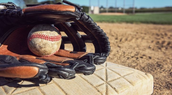 A baseball and a glove set atop a base on a baseball field